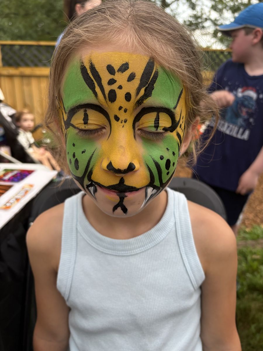 Girl with a full-face green and gold jungle cat design with black stripes, spots and painted fangs