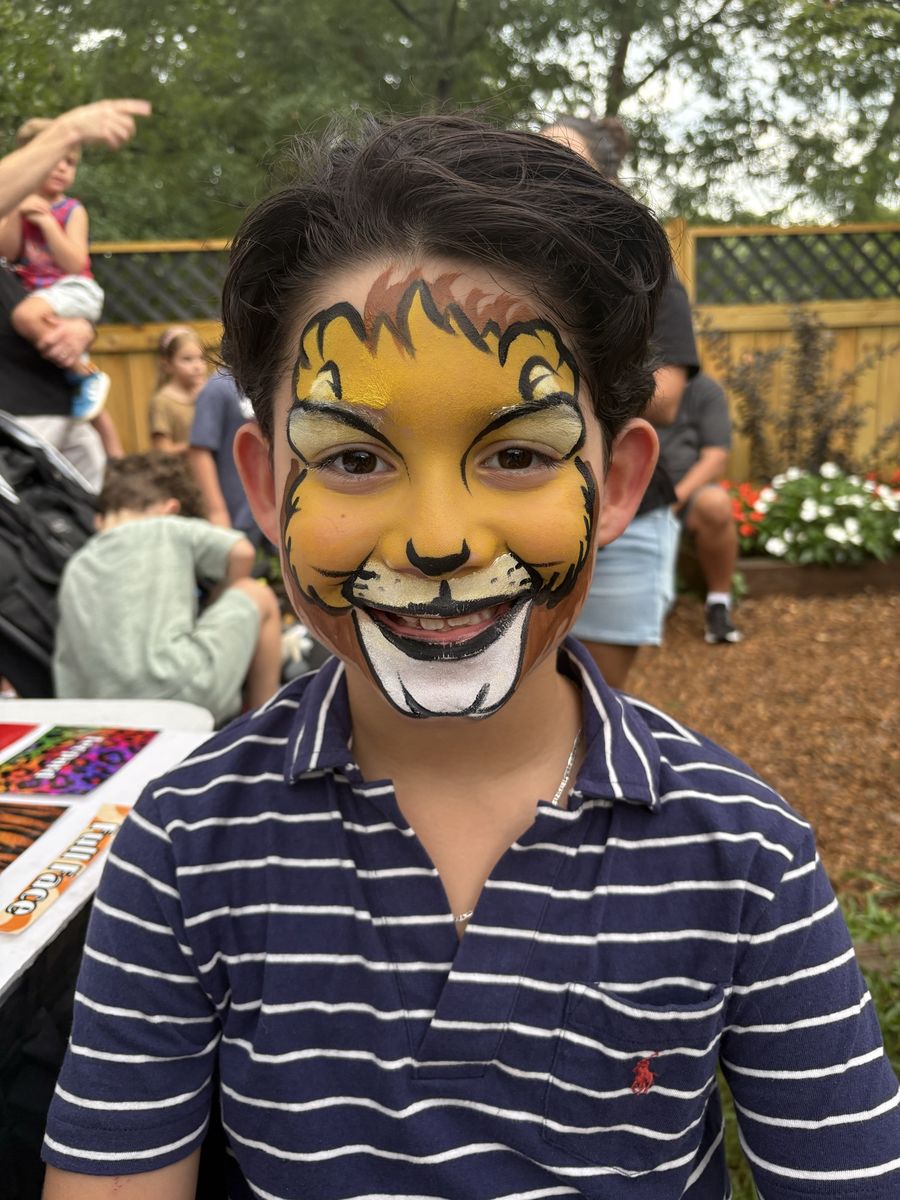 Boy smiling with a full-face golden lion design featuring a painted mane, whiskers and white muzzle