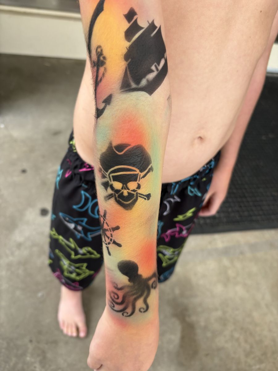 Airbrushed pirate arm sleeve with a galleon ship, skull and crossbones, ship wheel and octopus on a sunset background