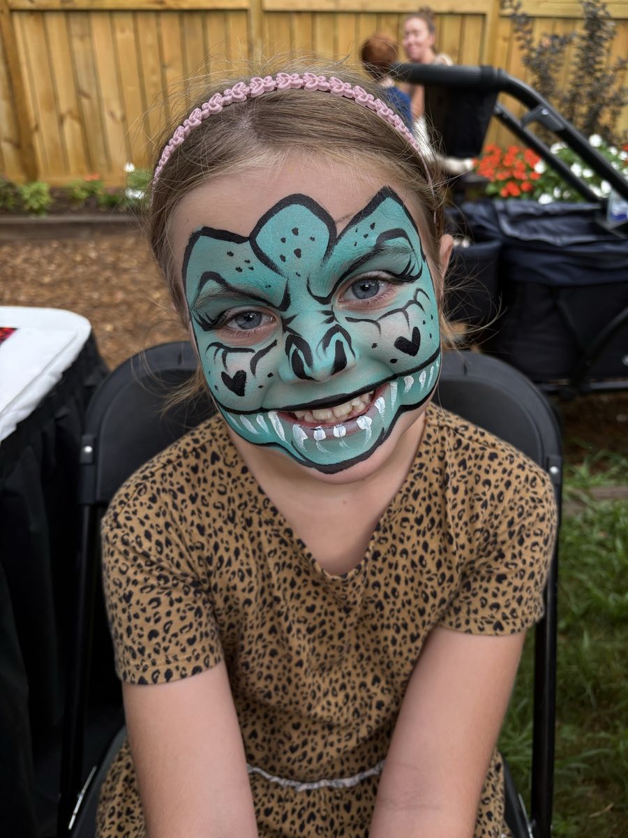 Girl in a leopard-print dress wearing a full-face teal dragon design with bold black linework and painted fangs