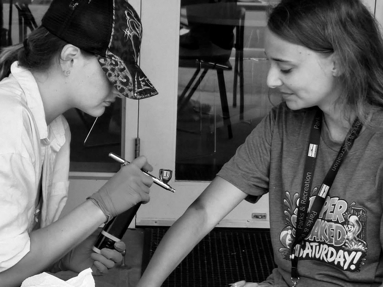 Kiwi Ink Creations artist airbrushing a design onto a guest's arm at an outdoor event